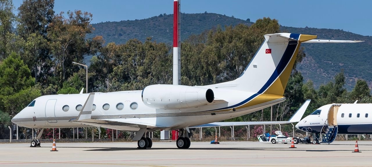 Bodrum yat limanına yaklaşan özel jet ve deniz kıyısındaki mavi bayraklı plaj manzarası.