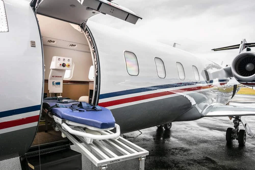 Yurt dışı tedavi için havalimanında ambulans jete taşınan bir hasta, refakatçileri ve sağlık personeli eşliğinde uçağa yönlendiriliyor.