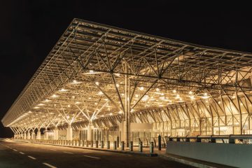 Addis Ababa Bole Havalimanı terminal binası ve önündeki yol, yeşil alanlar ve araçlarla birlikte genel dış cephe görüntüsü.