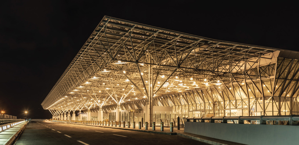 Addis Ababa Bole Havalimanı terminal binası ve önündeki yol, yeşil alanlar ve araçlarla birlikte genel dış cephe görüntüsü.