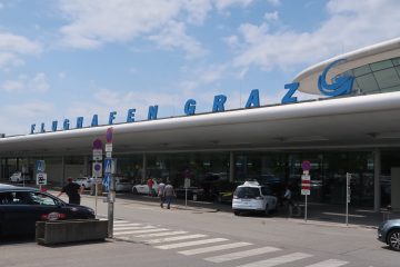 Avusturya Graz Havalimanı’nda (GRZ) pist kenarında Alpler manzarası eşliğinde park etmiş modern bir özel jet ve terminal binası.