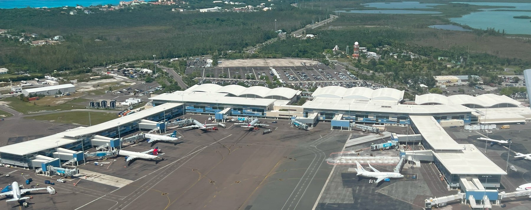 Bahamalar Nassau Havalimanı’nda (NAS) turkuaz deniz manzarasına yakın apron üzerinde park halinde modern bir özel jet ve terminal binası.