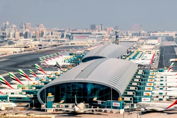 Dubai Havalimanı’nda (DXB) geniş terminal binası, yolcu köprülerine yanaşmış uçaklar ve hareketli apron manzarası