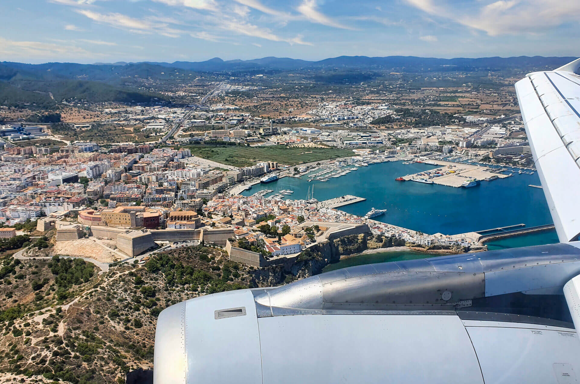 İspanya’da Ibiza’ya hizmet veren Ibiza Havalimanı terminal binası, önündeki “ibiza” yazılı mavi cephe, palmiye ağaçları ve yolcu alan araçlarla birlikte görülüyor.