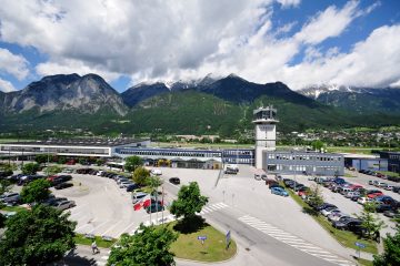 Avusturya Alpleri ile çevrili Innsbruck Havalimanı apronunda, karla kaplı dağların önünde park etmiş uçaklar ve terminal binası görülüyor.