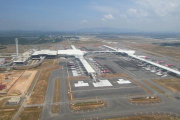 Kuala Lumpur Uluslararası Havalimanı terminal binası, önünde araçlar ve arkada kontrol kulesiyle birlikte gün batımında görüntüleniyor.
