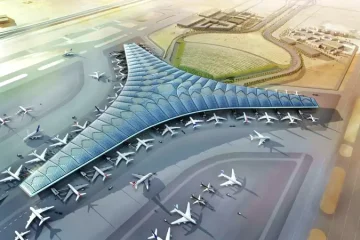 Kuveyt Uluslararası Havalimanı terminal binası, gece aydınlatmaları altında apron kenarında bekleyen uçaklar ve terminal önünde yolcu araçlarıyla birlikte görülüyor.