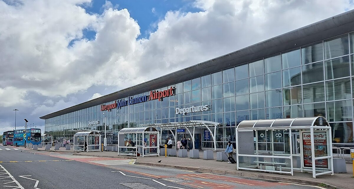 İngiltere’de Liverpool John Lennon Havalimanı terminal binası, önünde park etmiş bir yolcu uçağı ve apron üzerinde yürüyen yolcularla birlikte görüntüleniyor.