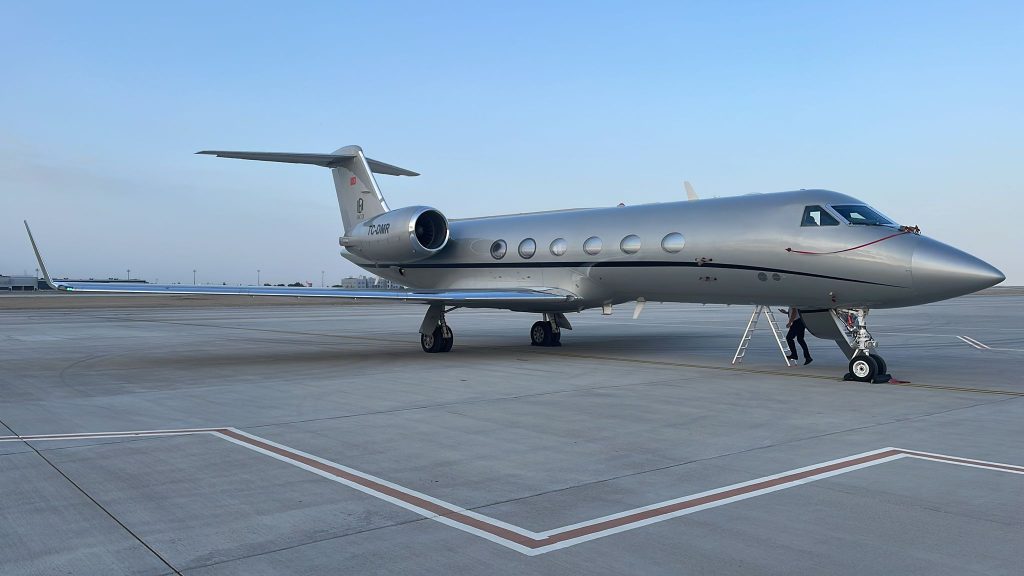Modern bir özel jetin önünde, seyahatine hazırlanan Aden Jet yolcusu ve ona eşlik eden yer ekibi.