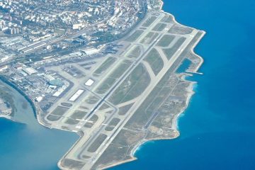 Nice Côte d'Azur Havaalanı’nda pistte bekleyen özel jet, Akdeniz kıyısı ve lüks yat limanı manzarasıyla birlikte gösteriliyor.