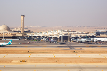 Riyad Kral Halid Havaalanı’nda pistte bekleyen özel jet, çöl manzarası ve modern terminal binasıyla birlikte gösteriliyor.