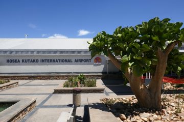 Namibya Hosea Kutako Havalimanı’nda (WDH) apron üzerinde park etmiş yolcu uçağı, terminal binası ve çevredeki kurak Afrika manzarası